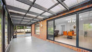 A covered patio area with a brick wall, large sliding glass doors leading to an interior dining space, and a ceiling with a metal framework. - The Canadian Escape, Ballarat - Up to 10 guests! (Canadian)