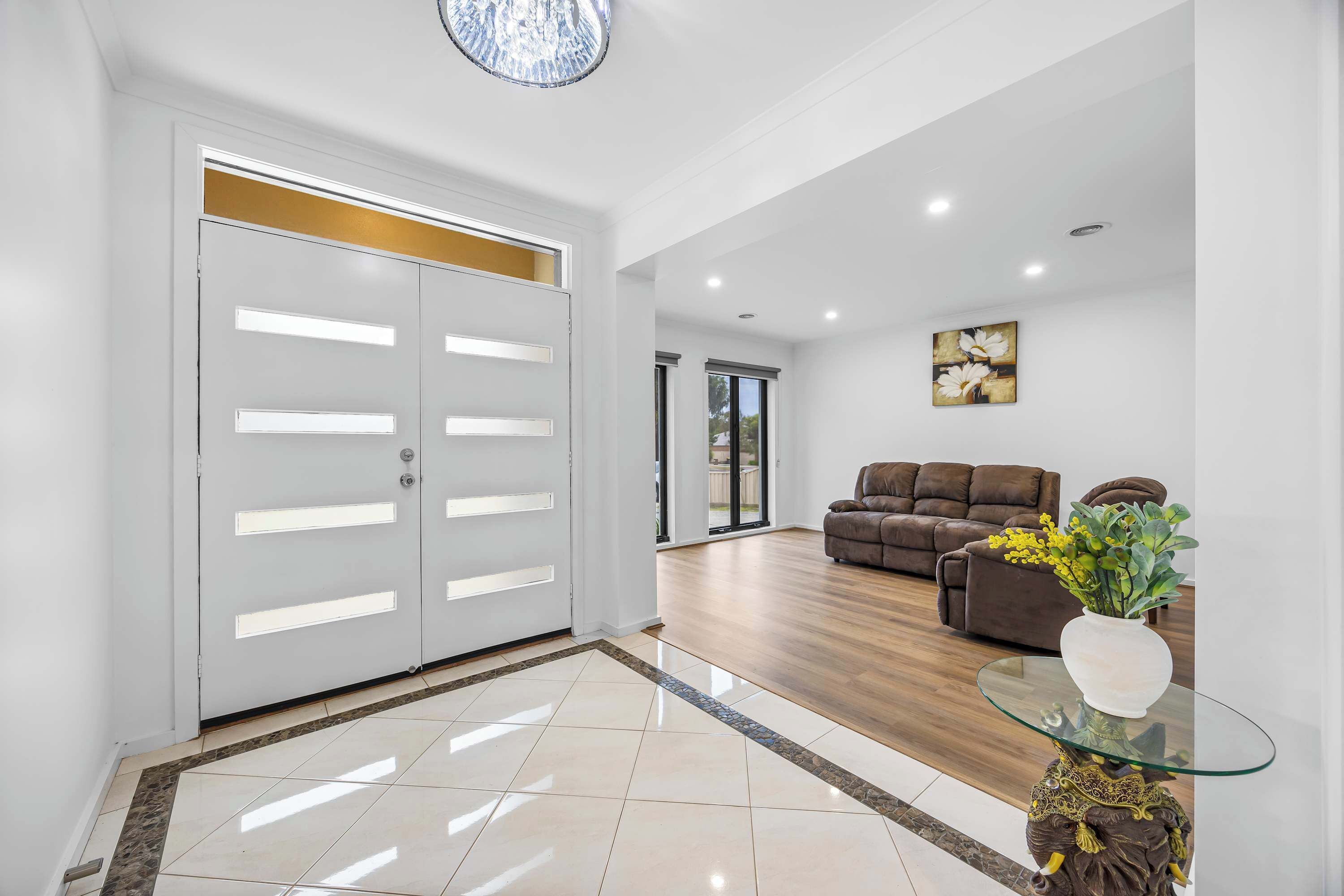 A spacious living area with a modern design, featuring a glass coffee table, a brown sofa, and a decorative vase.