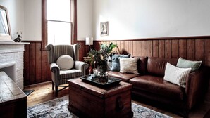 A cozy living room with a fireplace, a striped armchair, a brown leather sofa, and a wooden coffee table with a vase. - Kent House (Ballarat Central)