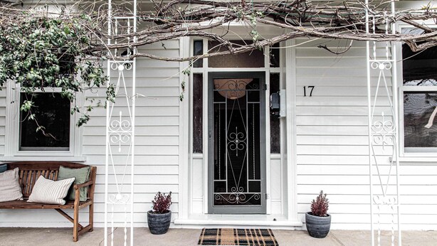 A white house with a black door, number 17, a bench, two potted plants, and a metal ladder. - Kent House (Ballarat Central)
