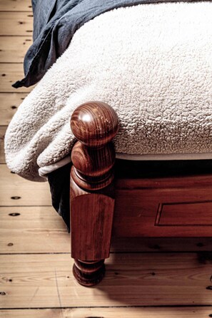 A wooden bed with a plush white cover, a dark blanket, and a wooden headboard.