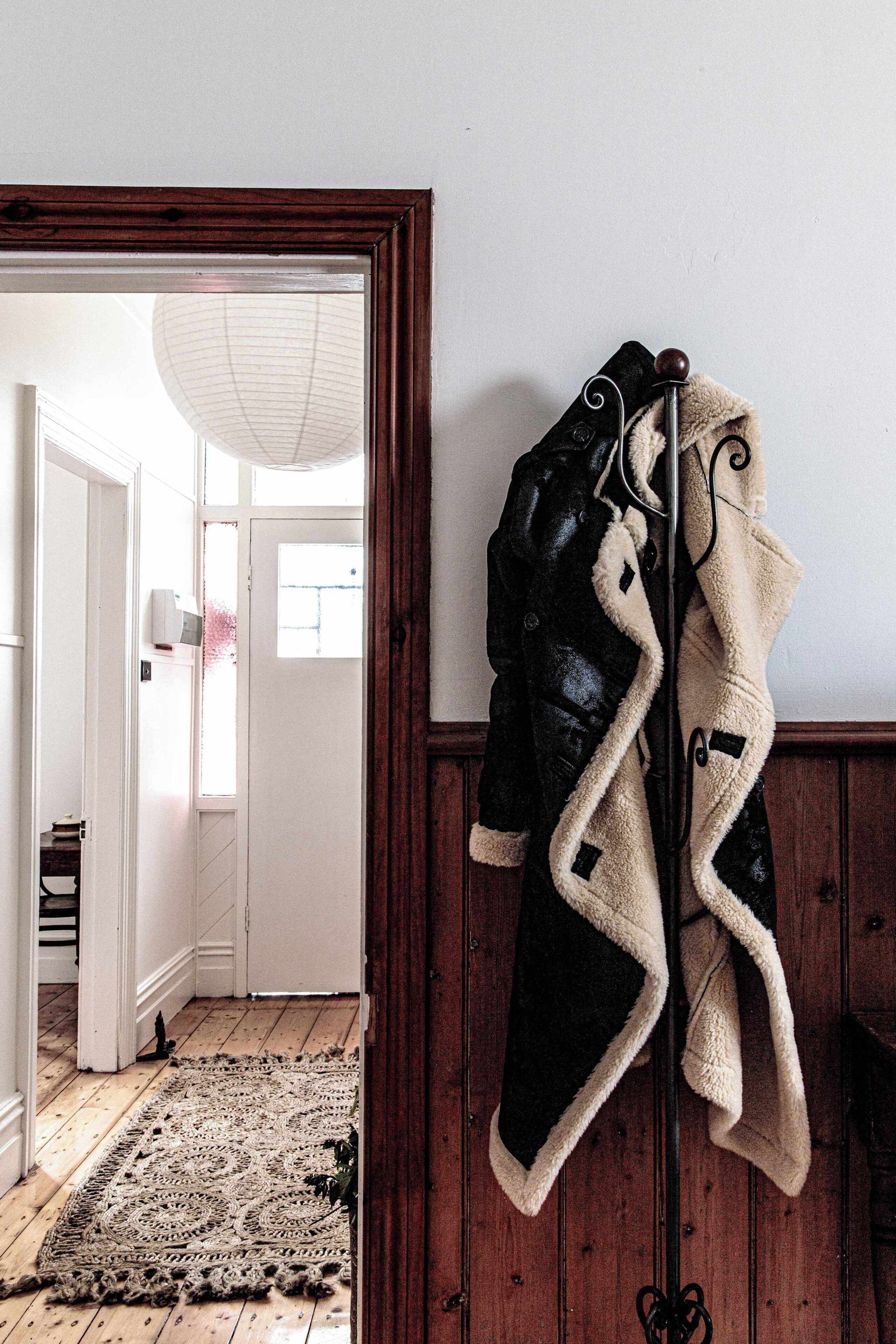 Una pared de madera con un perchero que sostiene dos abrigos. Un tapete con diseño cubre el suelo, y una puerta da a otra habitación.