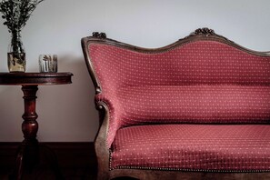 A red upholstered sofa with a curved backrest and decorative trim, positioned next to a wooden side table with a vase and candle. - Kent House (Ballarat Central)