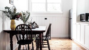 A kitchen with wooden flooring, white cabinets, a dining table with chairs, and hanging pendant lights. - Kent House (Ballarat Central)