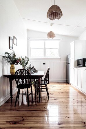 A kitchen with wooden flooring, white cabinets, a dining table with chairs, and hanging pendant lights.