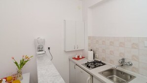 A small kitchenette with a gas stove, sink, and white cabinets. There is a coffee maker and a vase with flowers on the counter.