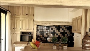 A kitchen with light wooden cabinets, a checkered backsplash, a fruit bowl on the counter, and a rustic metal container. - Le Belvedere-Charme de la Provence (Montauroux)