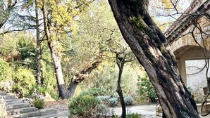 A stone pathway leading through a garden with mature trees and a stone building in the background. - Le Belvedere-Charme de la Provence (Montauroux)