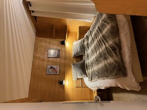 Une pièce avec un lit, un plancher en bois, un mur blanc et un tableau encadré.