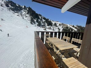 Une terrasse en bois avec une table et des chaises donnant sur une piste de ski enneigée.