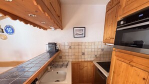 Een kleine keuken met houten kastjes, een zwart aanrecht, een betegelde achterwand, een vaatwasser en een koffiezetapparaat.