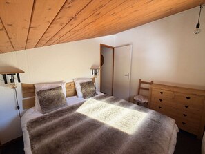 A bedroom with a wooden ceiling, a bed with a fluffy blanket, a nightstand with a lamp, and a wooden dresser with heart-shaped handles.