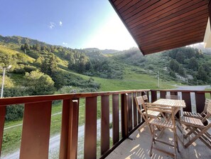 A balcony with a table and chairs, overlooking a mountainous landscape.