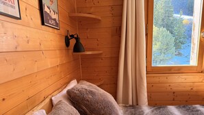 Een knus houten kamer met een bed, een wandlamp en een raam met gordijnen.