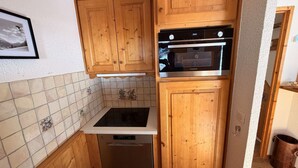 Een kleine keuken met houten kastjes, een inbouwoven en een vaatwasser.