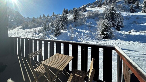 Een houten terras met een tafel en stoelen met uitzicht op een besneeerd berglandschap.