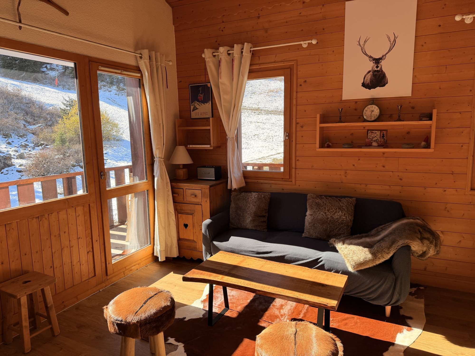 A cozy cabin interior with a wooden floor, a sofa, a table, and a window with curtains.