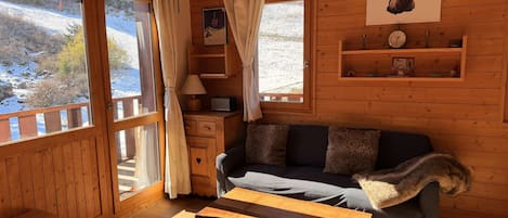 A cozy cabin interior with a wooden floor, a sofa, a table, and a window with curtains.