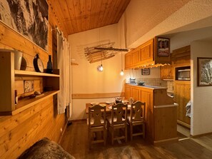 A cozy wooden interior with a dining table, chairs, and a kitchen area with wooden cabinets and a refrigerator.