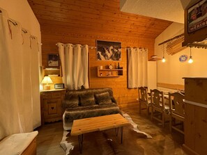 A cozy cabin interior with a wooden ceiling, a sofa, a table, and a dining area.