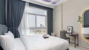 A modern bedroom with a large bed, a desk, and a view of the cityscape. - StayShort - Peaceful 1-Bedroom with Relaxing Balcony in Liwan! (Silicon Oasis)