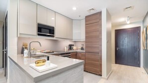 A modern kitchen with a central island, stainless steel appliances, and a dark wooden accent wall. - StayShort - Peaceful 1-Bedroom with Relaxing Balcony in Liwan! (Silicon Oasis)
