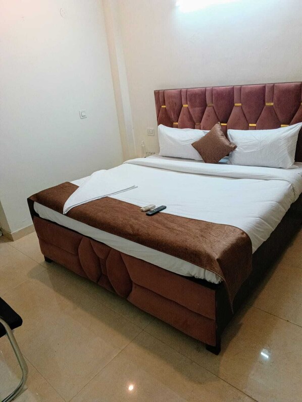 A neatly made bed with a brown headboard and white bedding, a remote control, and a bottle of water on the nightstand.