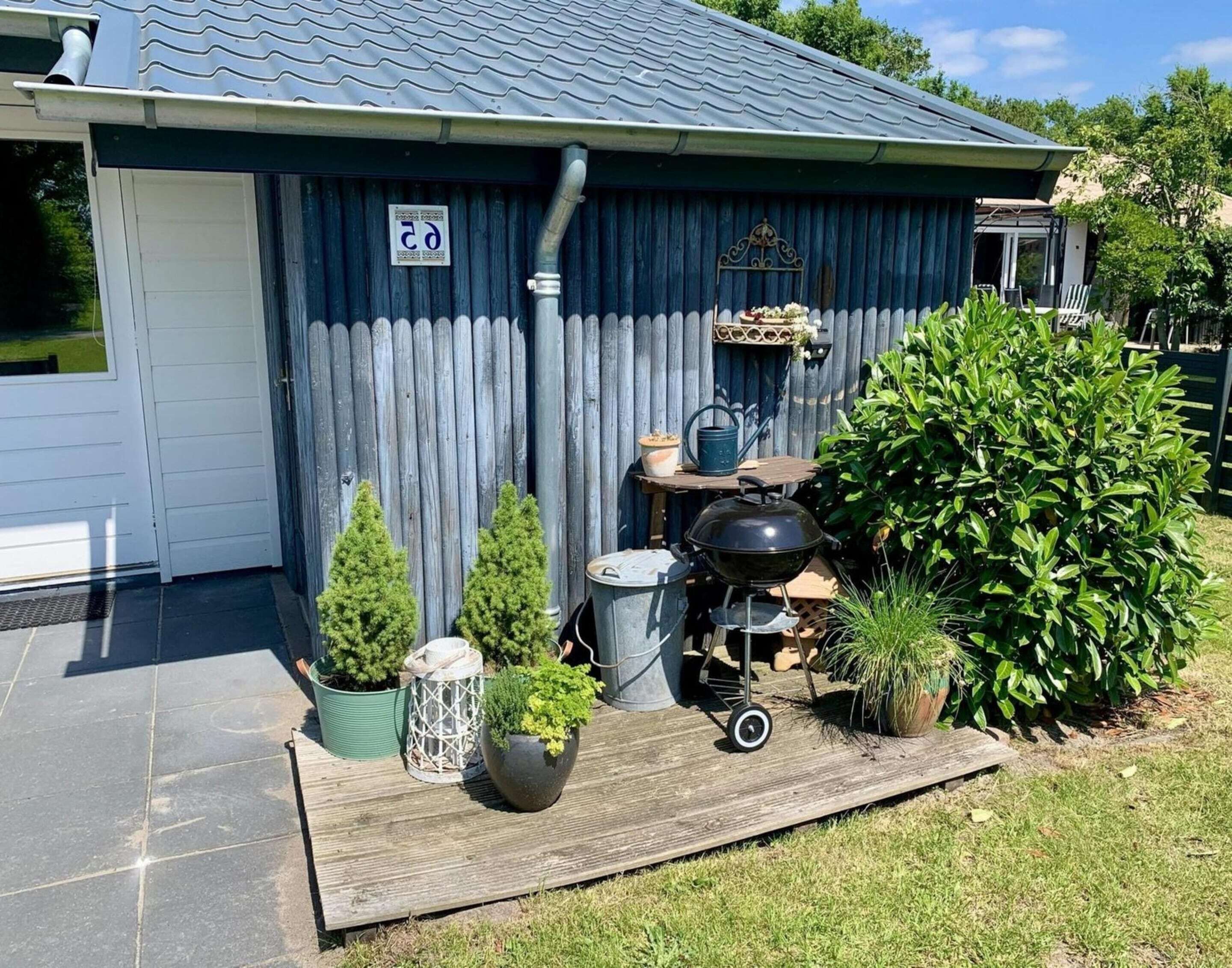 Un espace extérieur abrité comprenant un barbecue, des plantes en pot et une terrasse en bois.