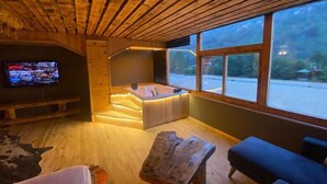 Een houten interieur met een televisie, een jacuzzi en uitzicht op de omgeving.