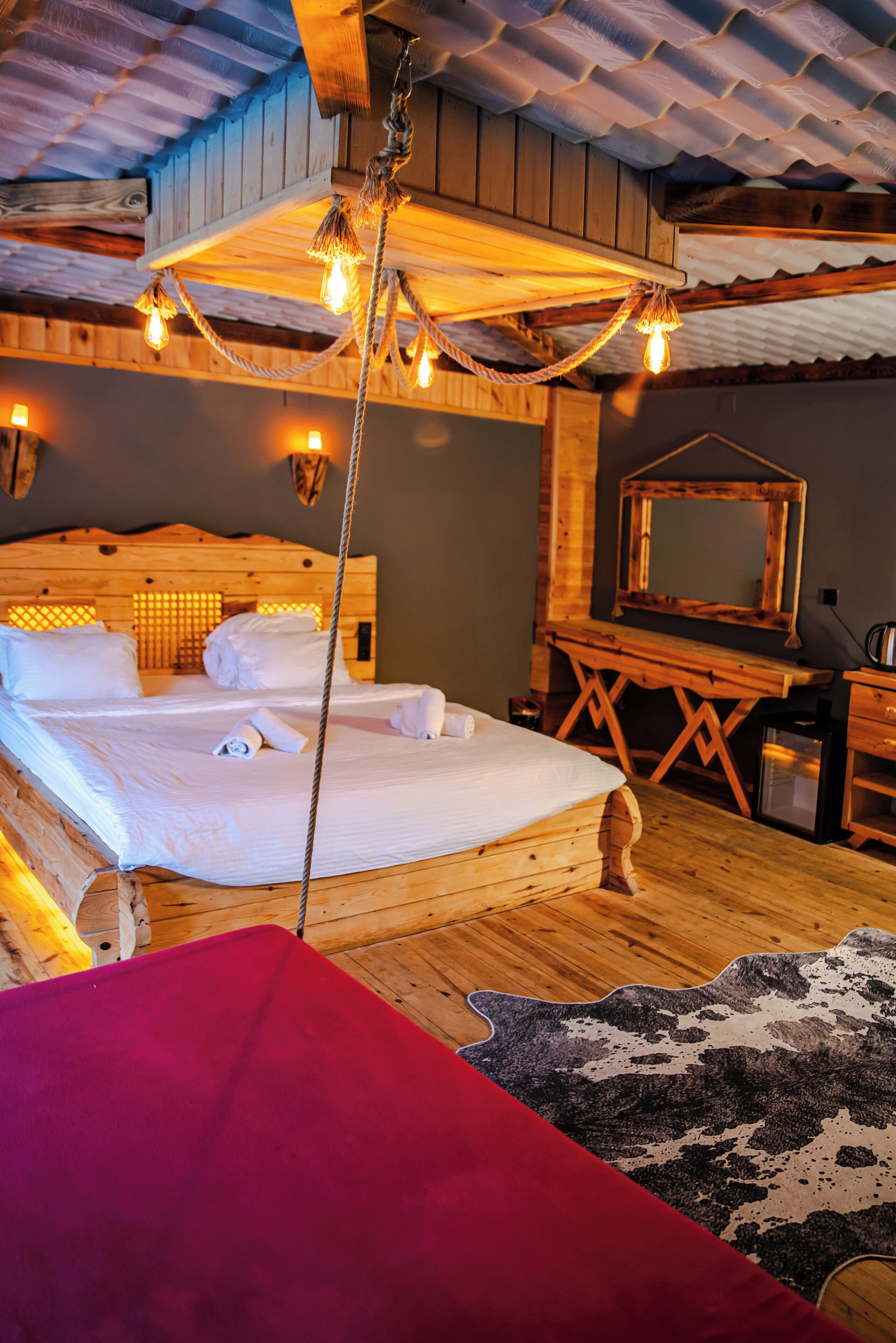A wooden room with a bed, a wooden desk, and a hanging light fixture.