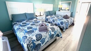 A bedroom with two beds, each with matching blue floral bedding and pillows. There is a nightstand with a lamp and a dresser with a mirror. - Cozy 1-bedroom condo with AC, WiFi in Terrific Myrtle Beach (Myrtle Beach)