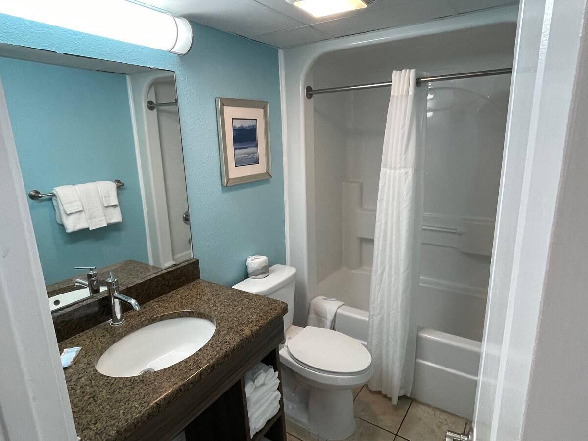 A bathroom with a granite countertop sink, a white toilet, and a glass shower enclosure.