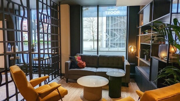 A modern lounge area with a sofa, two yellow armchairs, a round coffee table, and a bookshelf. - Student Only Merchant Studios in Glasgow (Glasgow)