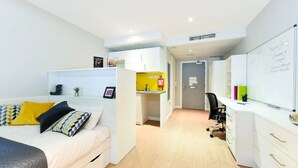 A modern, well-lit bedroom with a bed, a desk, and a kitchenette area. - Student Only Merchant Studios in Glasgow (Glasgow)