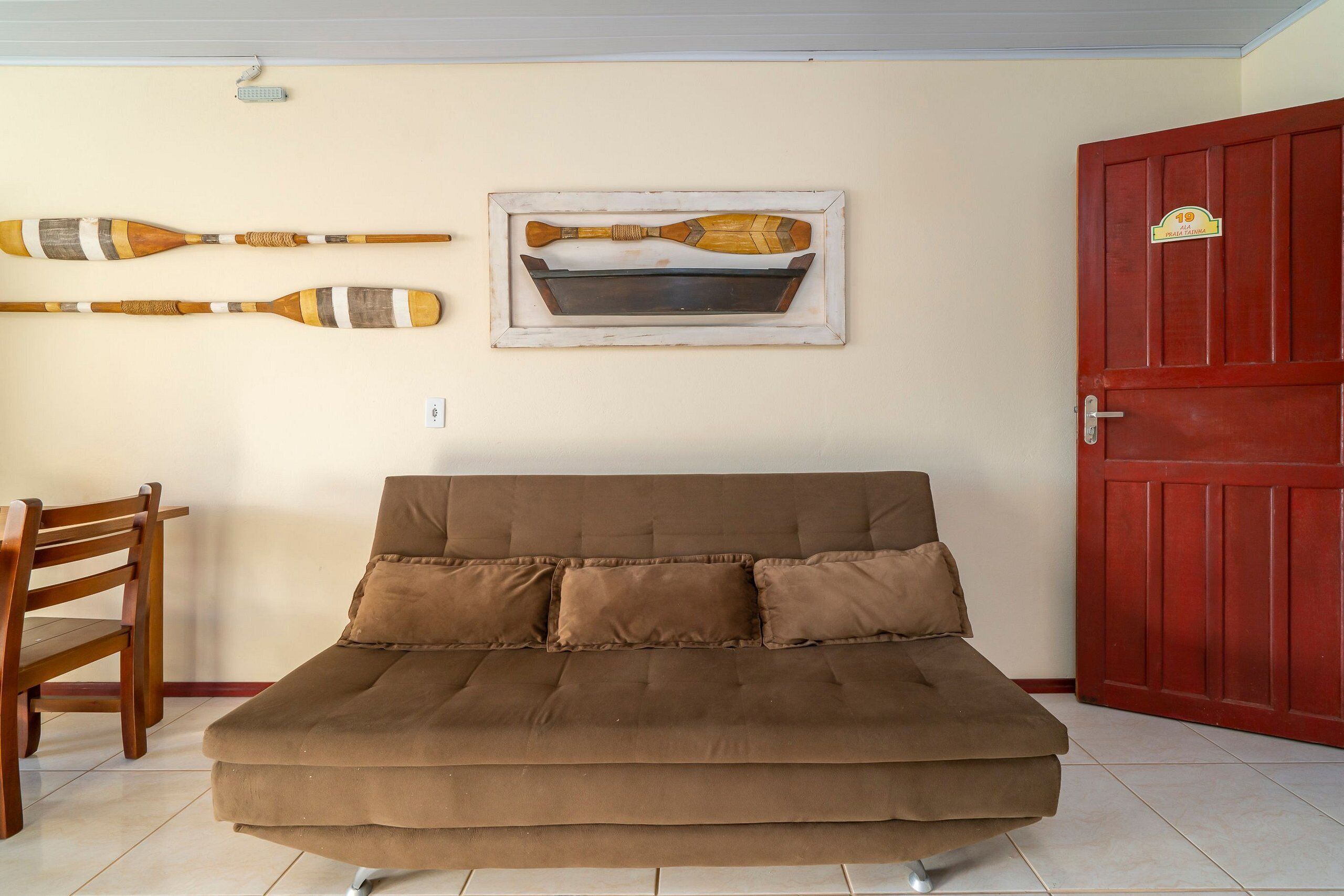 Una habitación con un sofá marrón, una silla de madera y un cuadro con unas palas en la pared.