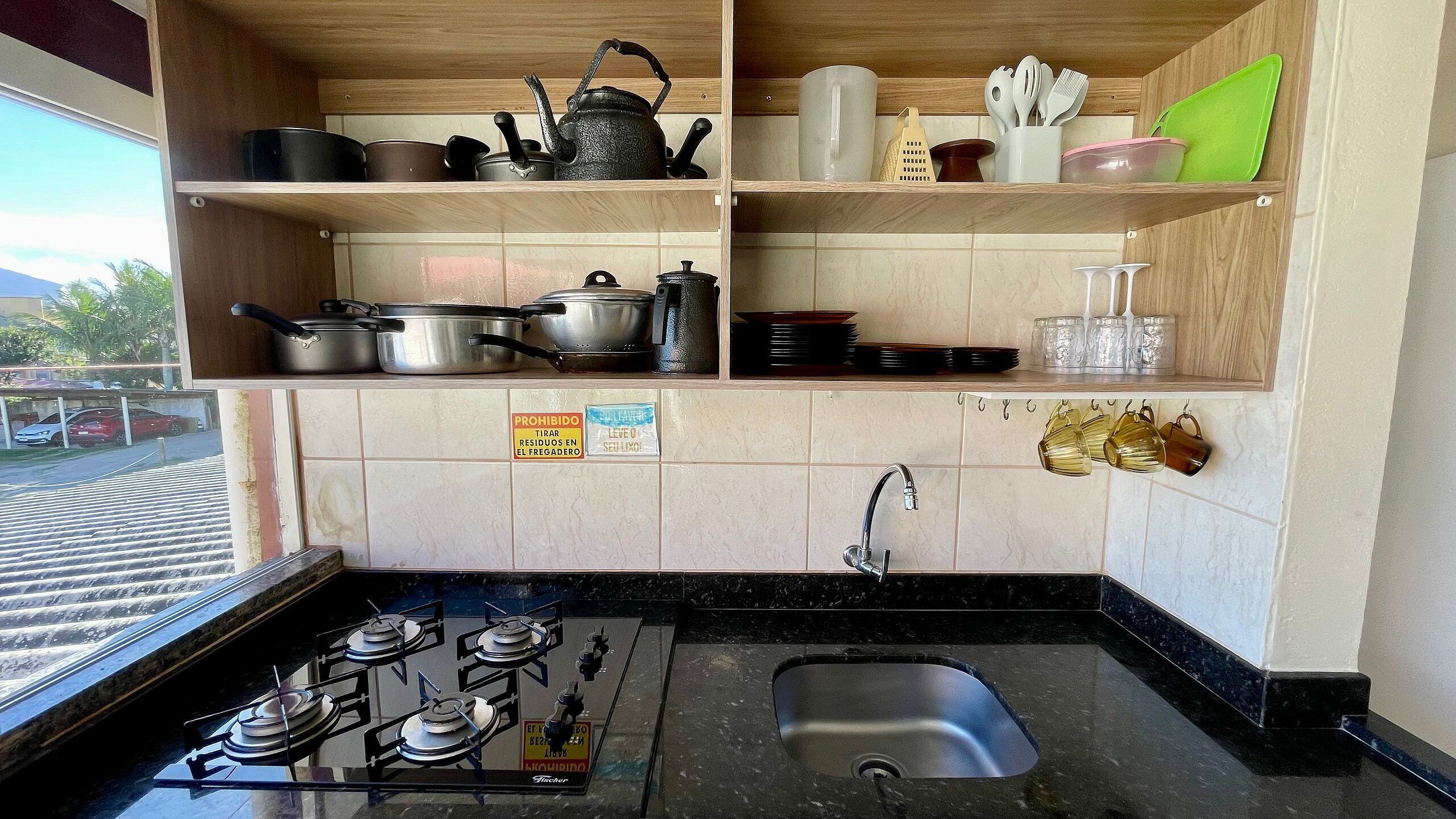 A kitchen with a gas stove, a sink, and various kitchen utensils and cookware on wooden shelves.