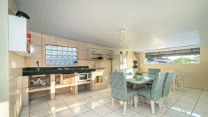 A kitchen with a dining area, featuring a tiled floor, a built-in oven, and a window with a view. - AP 20 Ala Tainha Residencial Solavir (Bombinhas)