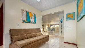 A spacious living area with a brown sofa, a dining area with chairs, and artwork on the walls. - AP 20 Ala Tainha Residencial Solavir (Bombinhas)