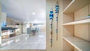A modern kitchen with white cabinets, a dining area with chairs, and a large window providing natural light. - AP 20 Ala Tainha Residencial Solavir (Bombinhas)