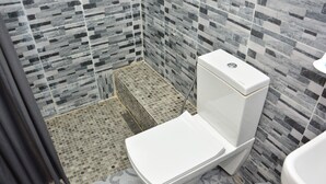 Une salle de bain avec un sol carrelé, des toilettes blanches et un espace douche.
