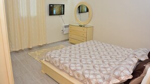 Une chambre à coucher avec un lit, une commode, un miroir et un téléviseur fixé au mur.