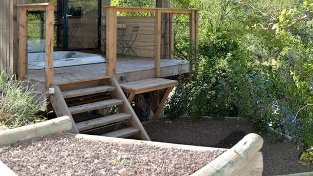 A wooden cabin with a balcony, a staircase leading up to the entrance, and a view of the surrounding forest. - Lodge Nid Perché - Les Cabanes de Provence (Lafare)