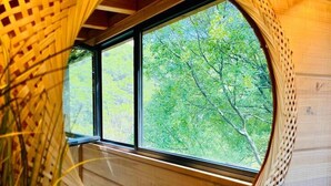 A circular wooden structure with a woven lattice design, a window, and a view of green trees. - Lodge Nid Perché - Les Cabanes de Provence (Lafare)