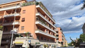 Un edificio de varios pisos con balcones, una tienda visible en la planta baja y un cielo despejado.