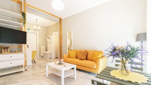 Una sala de estar moderna con un sofá, una mesa de centro y un televisor. Hay una planta y una lámpara sobre una mesa.