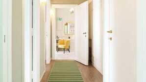 Un pasillo con alfombra verde a rayas, una silla amarilla y una puerta blanca que da a un baño.