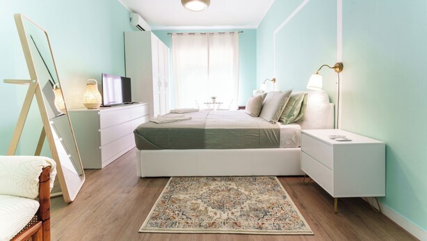 Un dormitorio con cama, mesitas de noche, escritorio, televisor y ventana con cortinas.
