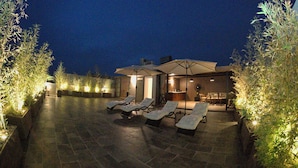 A patio with lounge chairs and a bar area, surrounded by potted plants.