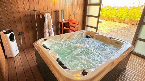 A hot tub in a wooden room with a view of a garden.