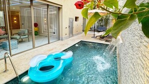 A swimming pool with a blue inflatable float, a glass door entrance, and a building with a beige facade.